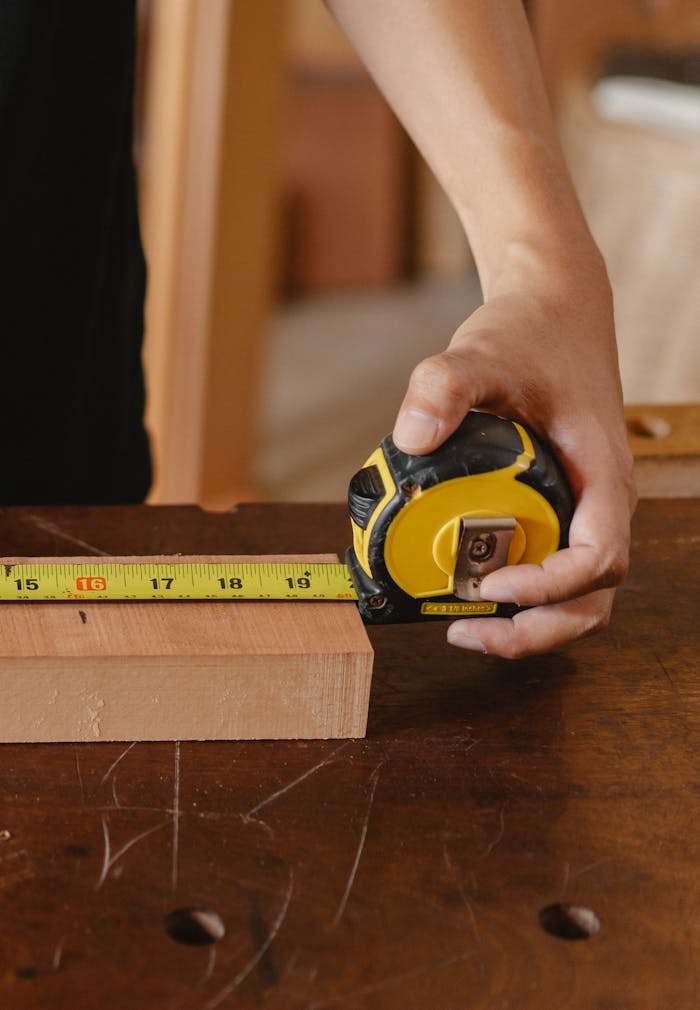 Close-up of carpenters hand measuring wood with a tape measure in a workshop.