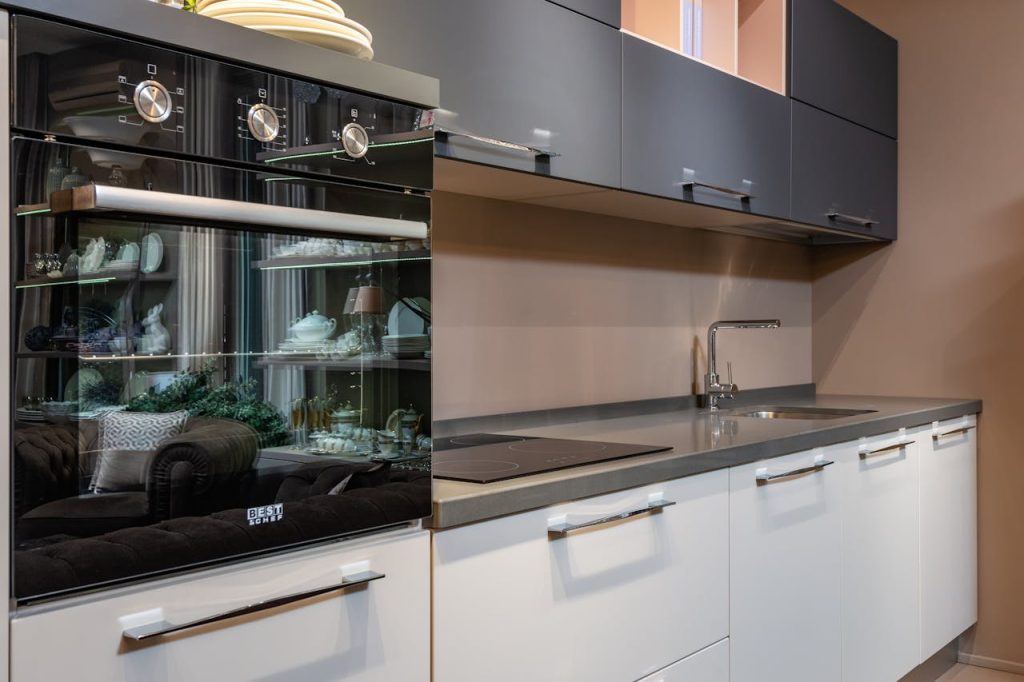 Modern black oven placed on counter with stove and sink in light stylish kitchen with white and gray cupboards in apartment
